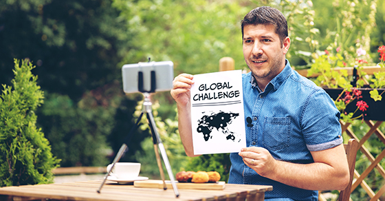 person posing in front of cell phone camera on tripod holding a paper that says global challenge
