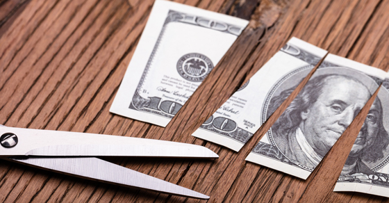 one hundred dollar bill cut into 4 equal pieces with open pair of scissors net to the pieces