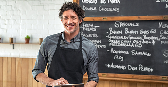 man in apron standing in front of chalkboard menu