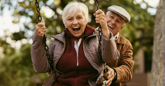 older gentleman pushing older woman on swing while both laughing