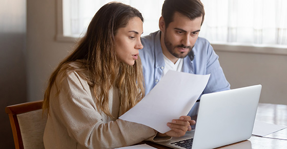 couple reviewing paperwork in front of open laptop