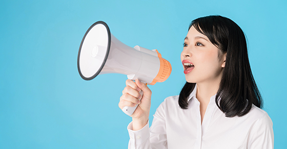 woman speaking into megaphone with solid blue background.