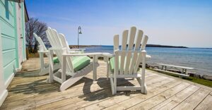 3 Adirondack chairs on a wooden deck overlooking a beach or coastal area