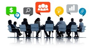 vector image of conference table surrounded by silhouettes of business people. Several people have conversation bubbles with icons representing charts, search icons, dollar signs, ideas 
