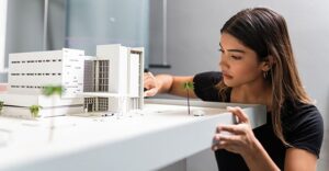 woman kneeling next to model size building complex situated on a table