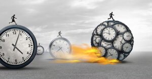 large stopwatches and clocks rolling across ground with people on top of them. One large ball of clocks with a person on it leads the rest and is on fire from moving so fast
