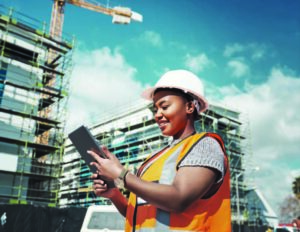 woman construction worker standing on construction site looking at tablet while smiling