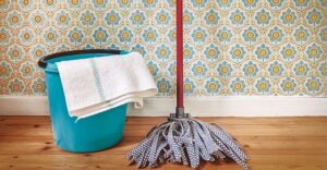 mop and bucket with folded towel hanging over the side against wall with 70s floral wallpaper print