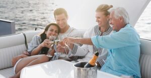parents with grown child and partner on boat, clinking glasses of wine while smiling and laughing