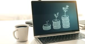 coffee cup sitting next to laptop with stacks of coins "growing"
