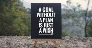 black easel on fallen tree that reads "a goal without a plan is just a wish"