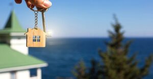 house shaped keychain being held in hand with lake house view behind