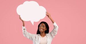 Positive African American woman with blank speech bubble on pink studio background, space for design. Lovely black lady with empty word box, mockup for your advertisement