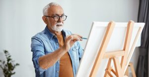 older gentleman painting at a standing easel