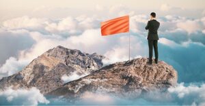 Leadership and success concept with thoughtful businessman and blank red flag on mountain top. Mock up