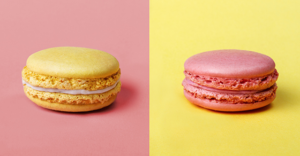 left side has pink background with single yellow macaroon cookie and right side has yellow background with single pink macaroon cookie.