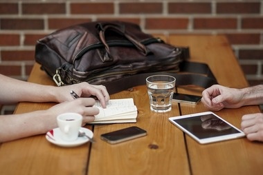 close up of hands of two people Having Business Meeting With Bag, Drinks And Technology on table