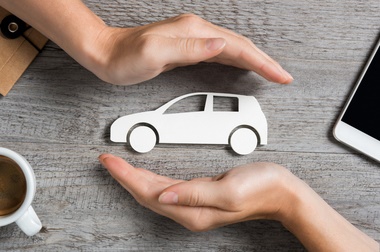 Hands protecting icon of car over wooden table. Top view of hands showing gesture of protecting car. Car insurance and automotive business, IRS Mileage deduction concept.