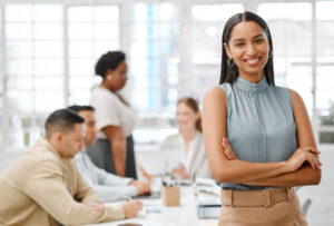 Smiling, happy and motivated young business woman/manager with arms crossed showing great leadership to her team in an office. Portrait of confident and proud entrepreneur satisfied with growth in a startup.