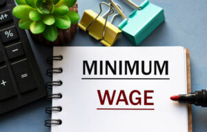 MINIMUM WAGE - word is written in a notebook with a marker, calculator, clamps and cactus
