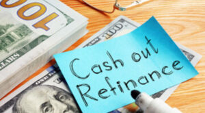 Cash out refinance is shown on piece of paper sitting on stack of hundred dollar bills