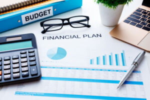 Financial plan concept with financial report used to prepare budget. Calculator and pen sitting on desk next to financial plan, glasses folded and sitting above financial plan