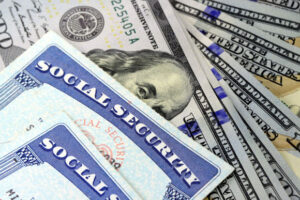 close up of corner of social security card placed over stack of fanned out hundred dollar bills