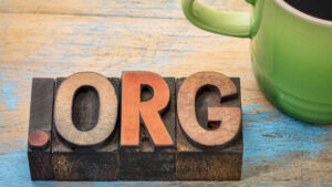 The word "org" is written in wooden letterpress type on a wooden table next to a green cup of coffee. This could be interpreted as a metaphor for the word "organization."