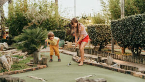 Group of two funny kids playing mini golf, children enjoying a family vacation