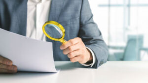 businessman or tax inspector analyzing document with magnifying glass in office. business financial audit concept. Analyzing for fraud