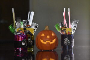 two halloween candle holders filled with candy placed on a table with a small jack o lantern between them.