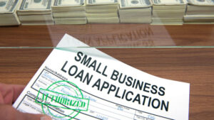Approved small business loan application in front of bank window lined with stacks of cash
