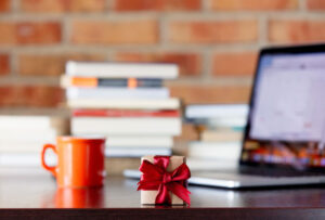 little gift box on a table with laptop computer and books on brick wall background indicating an employee gifts


