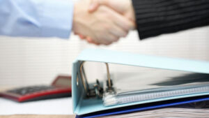 handshake over binder of documents to signal outsourced contract for accounting services
