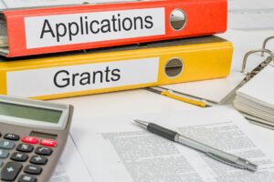 Folders with the label Applications and Grants along side a pen sitting on a grant application.