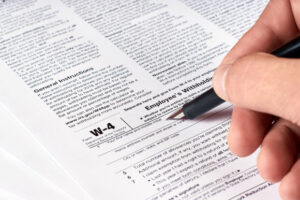 human hand fills out the W-4 tax form for income tax withholdings