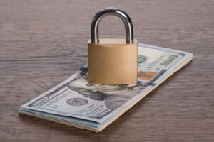 padlock sitting on top of stack of hundred dollar bills on a wood surface to indicate restricted funds
