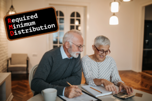 Older couple sitting at dining room table looking over their retirement documents with a sign in the upper corner that reads Required Minimum Distributions. The couple looks happy while doing their retirement planning.