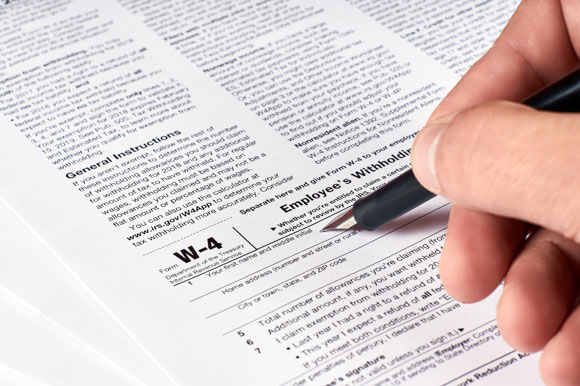 human hand fills out the W-4 tax form to show exemptions