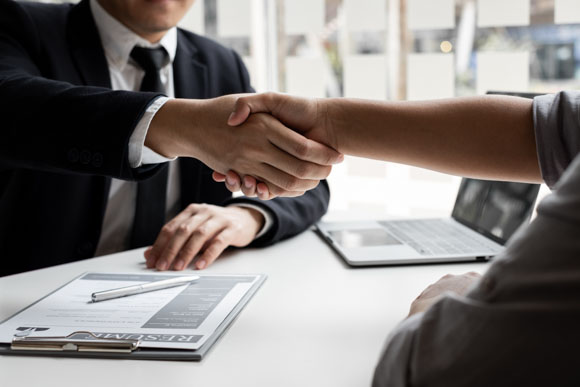 close up of business owner shaking hands over a compensation plan and resume of a new hire.