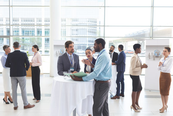 Business networking event with high-top tables and people scattered around the venue mingling and talking, demonstrating proper business etiquette
