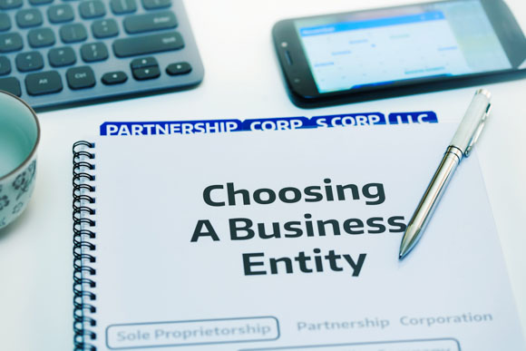 Startup company desk reviewing the different types of business entities. Binder with tabs on each type of entity. S Corporation is indicated as the preferred choice in this scenario