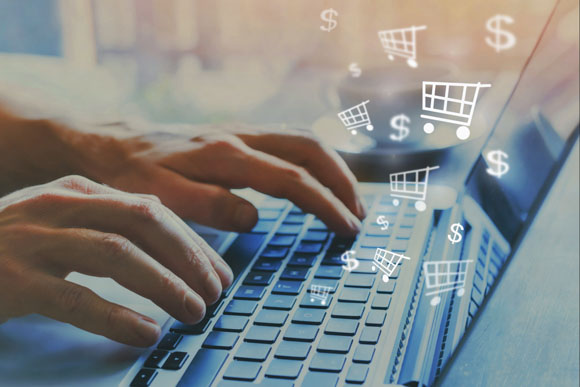 hands over keyboard of laptop with shopping cart and dollar sign icons floating over indicating participating in e-commerce by shopping online