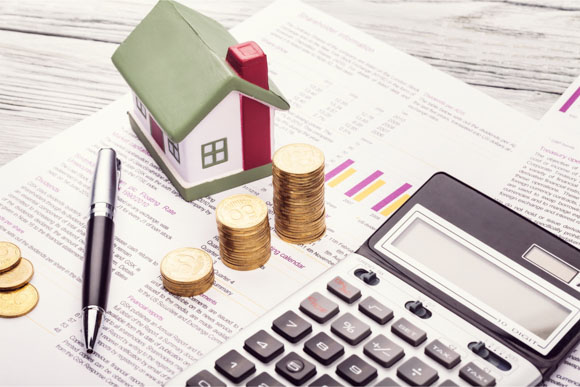 A financial planning setup featuring stacked coins, a calculator, and a model house on top of financial documents—symbolizing smart money management for stable living.