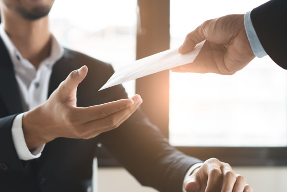 A professional handing an envelope to a colleague, symbolizing payroll processes and the importance of timely and accurate employee compensation.