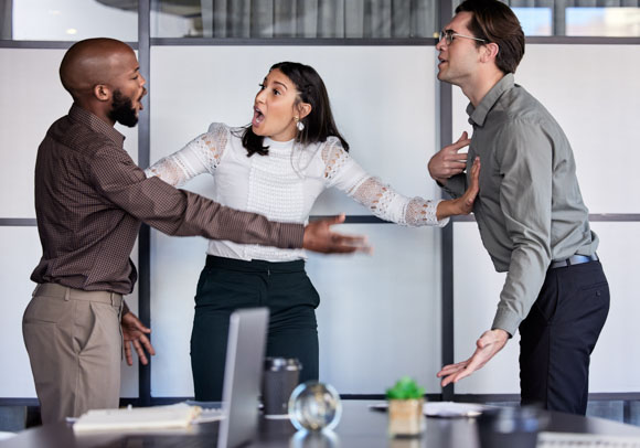 A workplace conflict escalates as two male colleagues engage in a heated argument, while a female coworker attempts to de-escalate the situation. The tense office scene highlights the importance of preventing workplace violence through conflict resolution and safety measures.